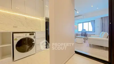 Modern apartment with sleek kitchen and cozy living room, featuring a washing machine and stylish decor.
