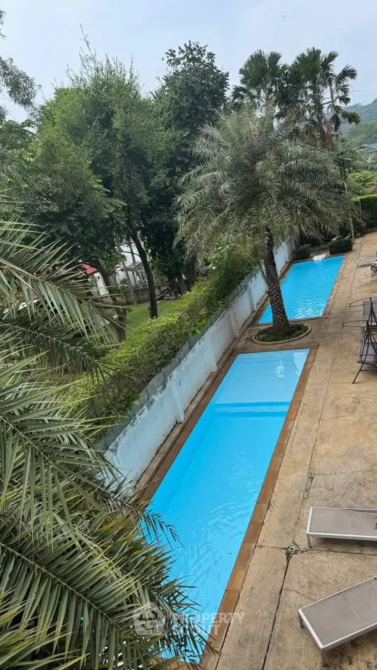 Luxurious outdoor pool area with lush greenery and palm trees, perfect for relaxation.