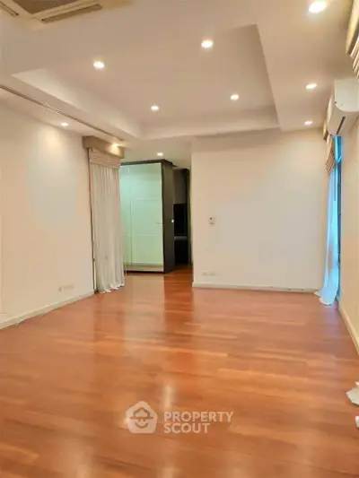 Spacious empty room with wooden flooring and recessed lighting, ideal for customization.