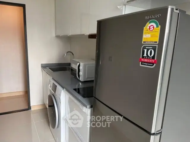 Modern kitchen with sleek appliances including fridge, washing machine, and microwave in compact layout.