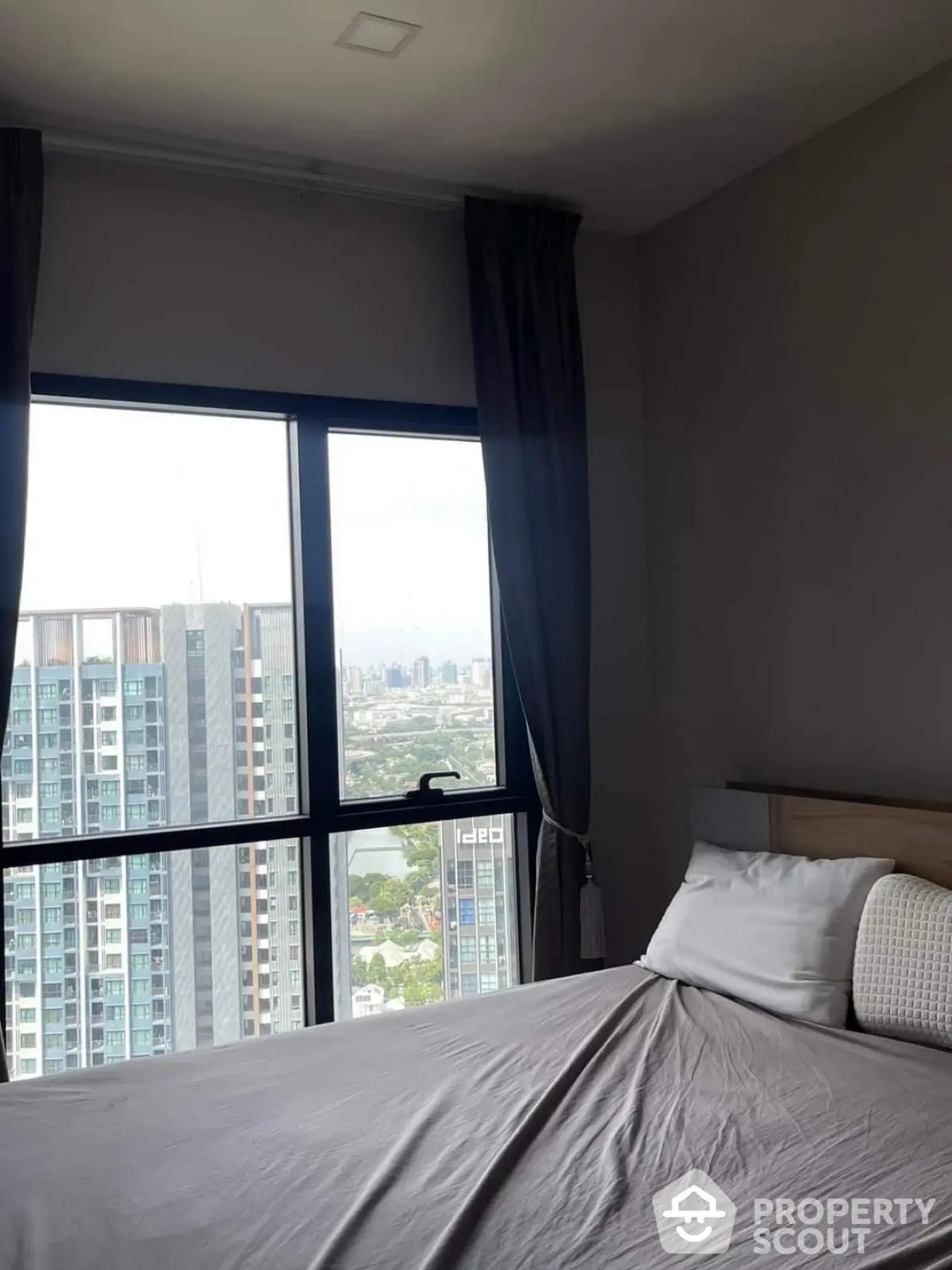 Modern bedroom with large window offering stunning city view in high-rise apartment.