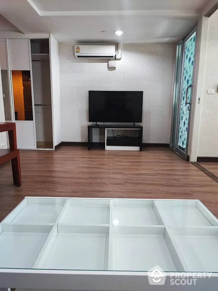 Modern living room with sleek furniture and wooden flooring, featuring a flat-screen TV and air conditioning.