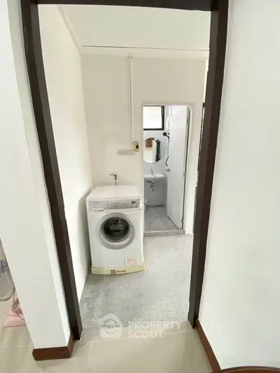 Compact laundry area with washing machine leading to a bathroom.