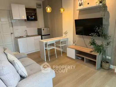 Modern living room with cozy sofa, wall-mounted TV, and compact kitchen area.