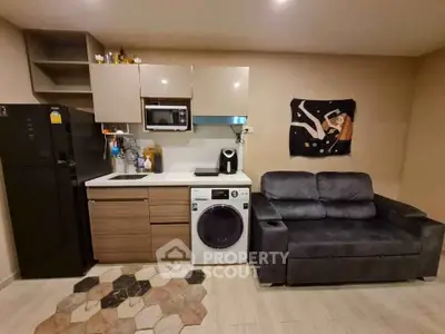 Modern compact kitchen with washing machine and cozy sofa in open layout.