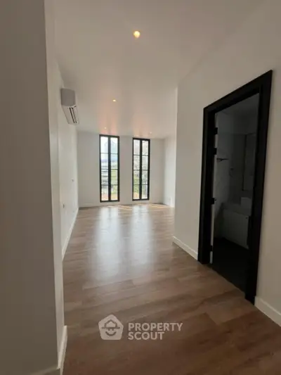 Spacious and bright living area with high ceilings, large windows offering natural light, and elegant wooden flooring, perfect for modern living.