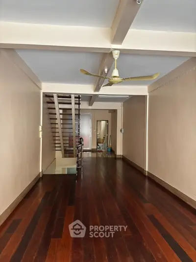 Spacious interior with wooden flooring and ceiling fan, featuring a staircase and mirror for modern living.