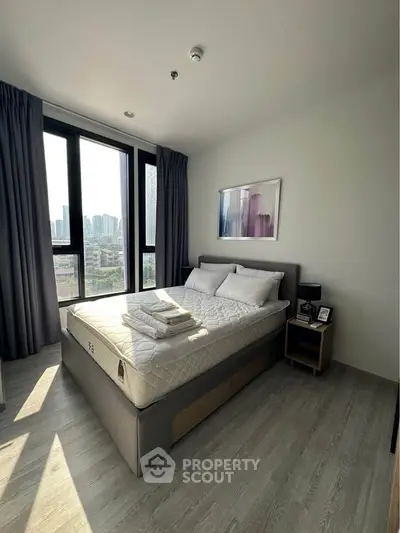 Modern bedroom with large windows and city view, featuring a stylish bed and elegant decor.
