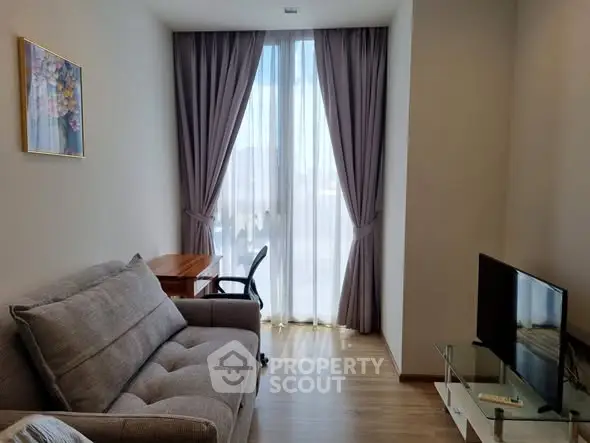 Cozy living room with modern sofa, desk, and TV, featuring floor-to-ceiling window with elegant curtains.