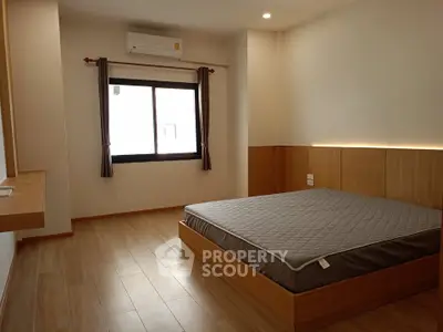Spacious bedroom with wooden flooring and large window in modern apartment.
