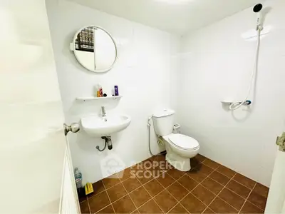 Modern bathroom with white tiles and brown floor, featuring a round mirror and essential fixtures.