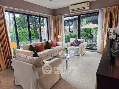 Spacious living room with large windows and garden view, featuring elegant sofas and modern decor.