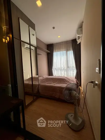 Cozy bedroom with wooden flooring, mirrored wardrobe, and natural light from large window.