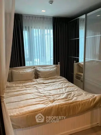 Cozy bedroom with elegant bedding and large window offering city views, perfect for relaxation.