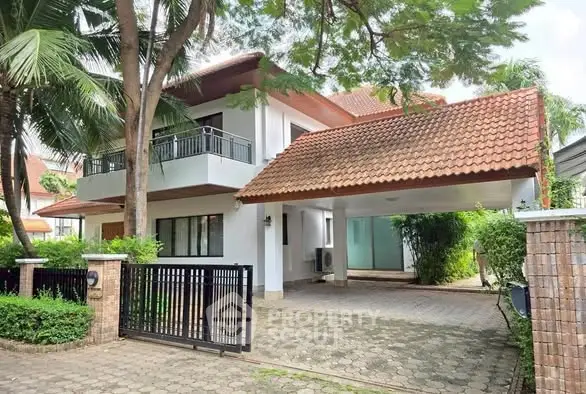 Charming two-story house with tiled roof and spacious driveway in lush green setting.