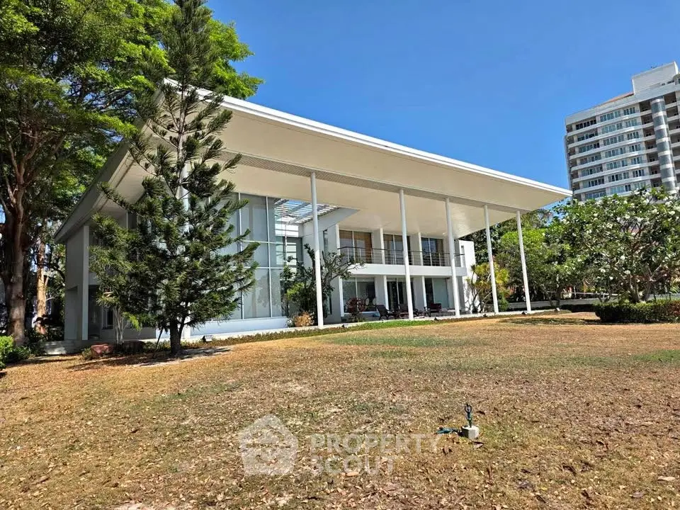 Modern architectural masterpiece with sleek lines and expansive windows, surrounded by lush greenery and clear blue skies.