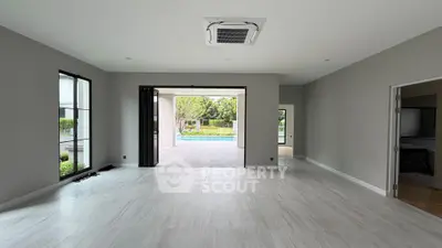 Spacious modern living room with open view to lush garden and pool area, featuring sleek flooring and large windows.