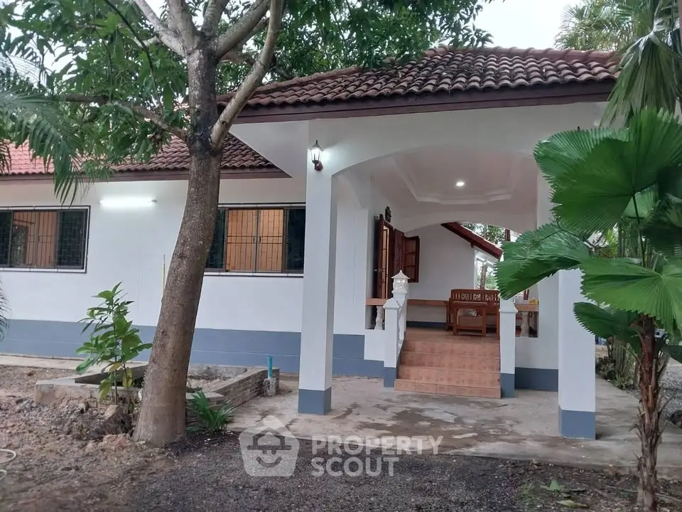 Charming single-story home with tiled roof and inviting front porch in lush garden setting.