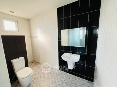 Modern bathroom with sleek black and white tiles, featuring a toilet and wall-mounted sink.