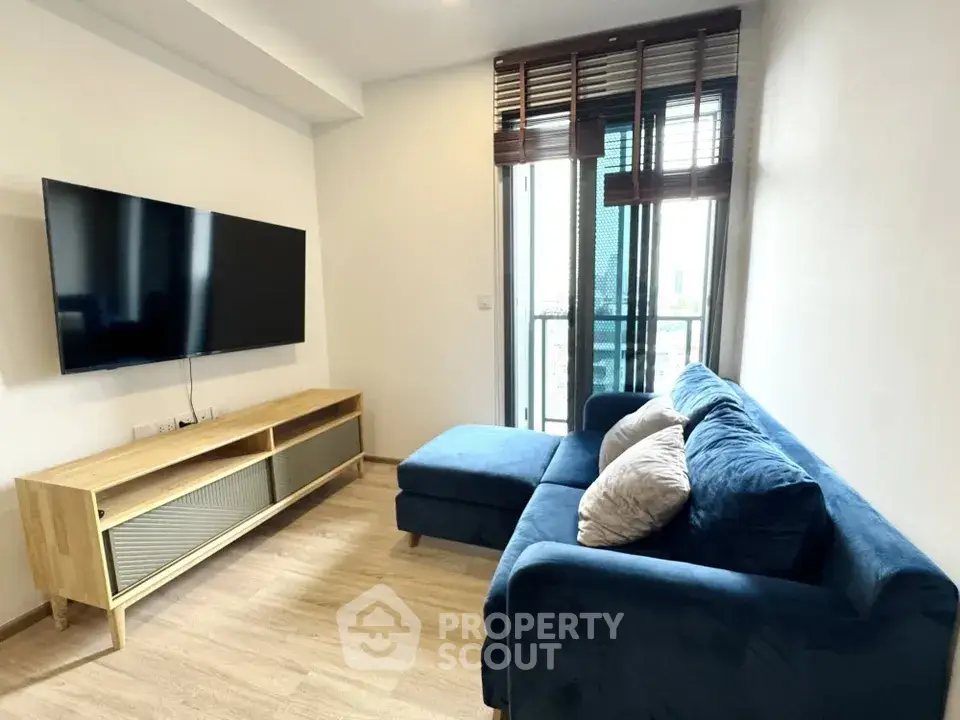 Modern living room with blue sofa and wall-mounted TV, featuring a sleek wooden floor and natural light.
