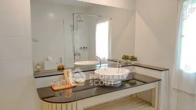 Elegant bathroom with modern fixtures and large mirror, featuring a sleek countertop and glass shower enclosure.
