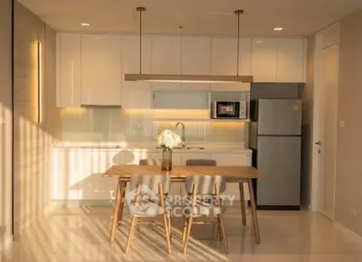 Modern kitchen with sleek cabinetry, dining table, and stainless steel appliances in a sunlit apartment.