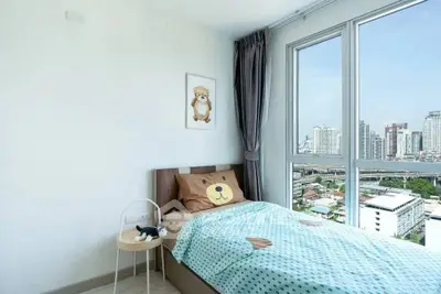 Bright bedroom with large window offering stunning city view, featuring cozy bear-themed bedding and modern decor.