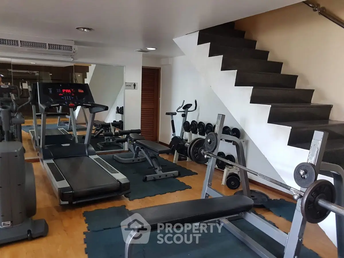 Modern home gym with treadmill, weights, and bench under sleek staircase