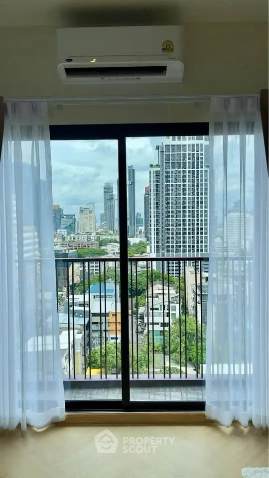 Stunning city view from modern apartment balcony with floor-to-ceiling windows and sheer curtains.