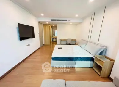 Spacious modern bedroom with wooden flooring and wall-mounted TV in a stylish apartment.