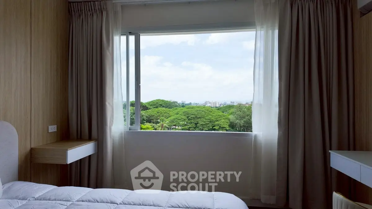 Bright bedroom with large window offering stunning green view.