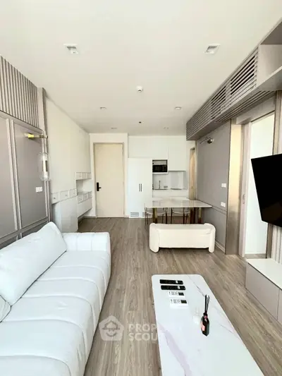 Modern living room with sleek design, featuring a white sofa, stylish coffee table, and open kitchen layout.