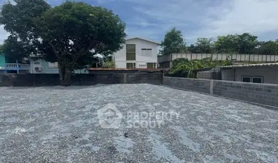 Spacious gravel lot with potential for development, surrounded by greenery and residential buildings.