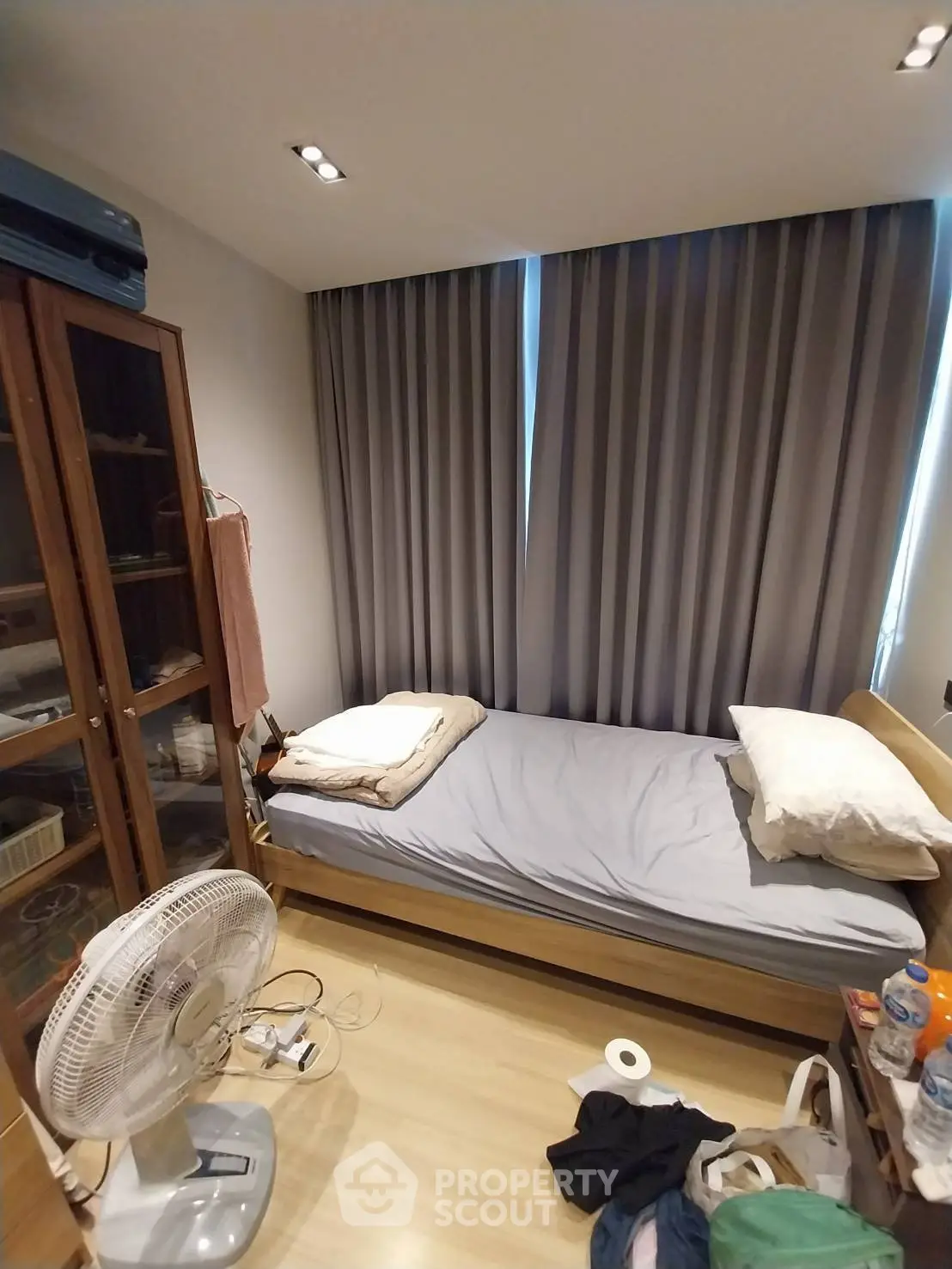 Cozy bedroom with single bed, wooden flooring, and large window with curtains.
