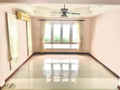 Spacious living room with large windows and ceiling fan, perfect for natural light and comfort.