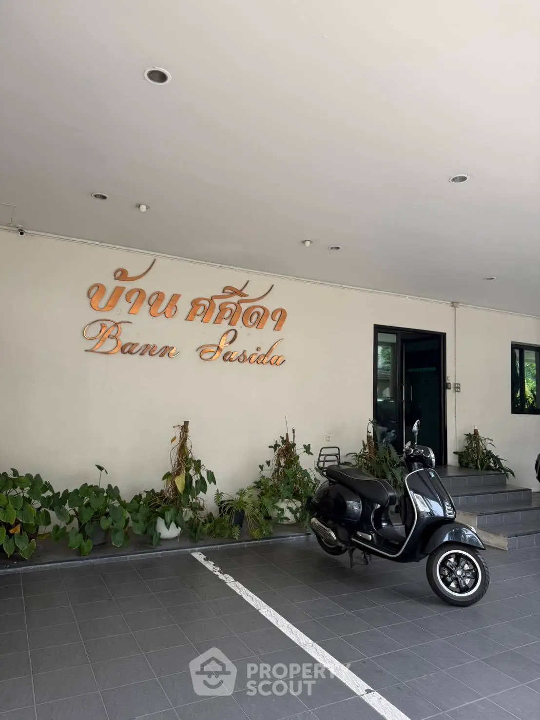 Charming entrance of Bann Susida with scooter parked, showcasing modern design and greenery.
