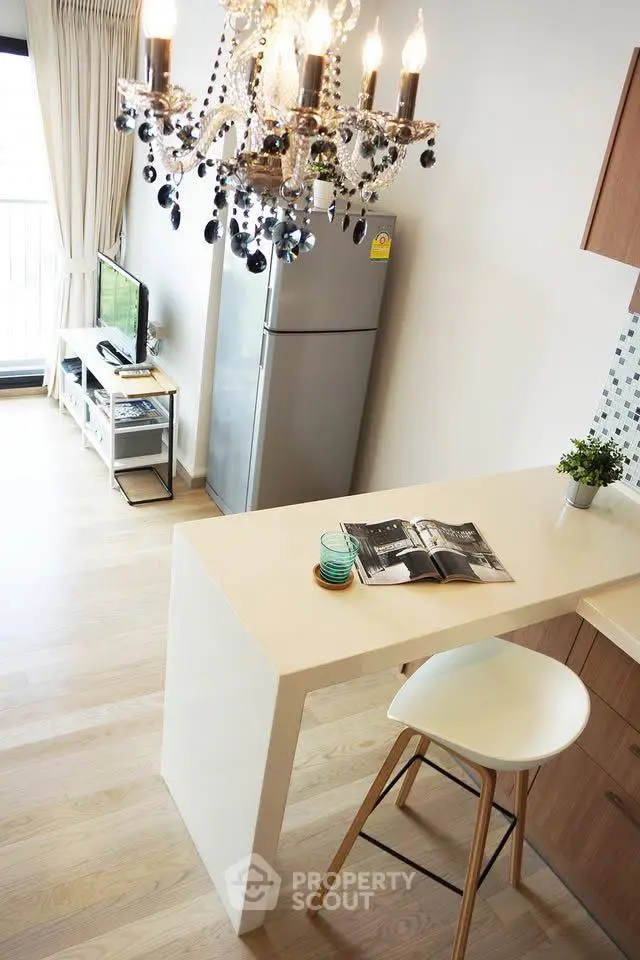 Modern kitchen with elegant chandelier and open layout, featuring a sleek fridge and stylish bar seating.