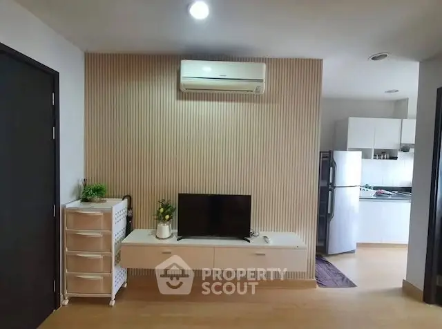 Modern living room with TV, air conditioning, and view into a sleek kitchen area.