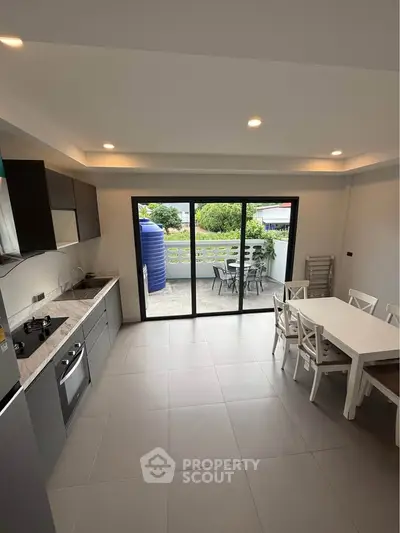 Modern kitchen with open layout and dining area leading to a spacious balcony with outdoor seating.