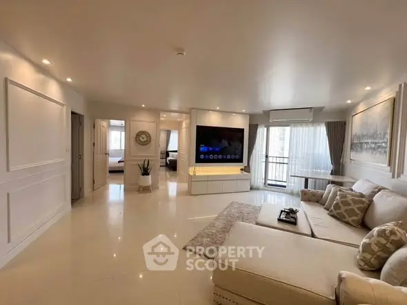 Spacious modern living room with elegant decor and large TV, leading to a cozy bedroom.