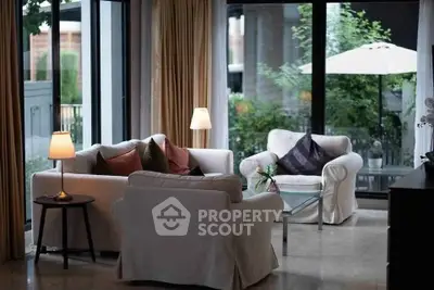 Elegant living room with cozy seating and large windows overlooking a lush garden patio.