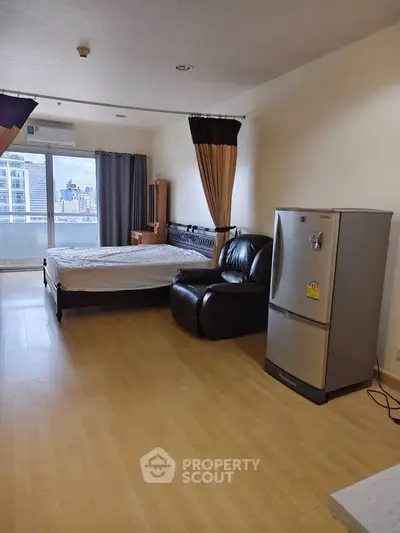 Spacious studio apartment with city view, featuring modern furnishings and a large refrigerator.