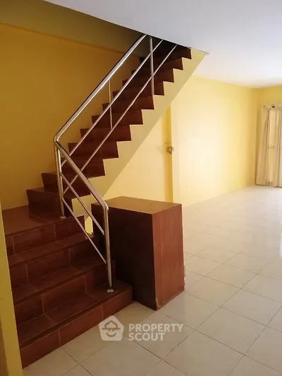 Spacious interior with tiled flooring and modern staircase in a bright yellow-painted room.