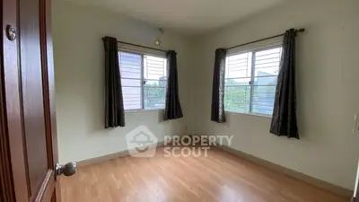Bright empty bedroom with wooden floor and large windows in a cozy home.