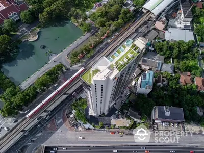 Aerial view of modern high-rise building with rooftop pool and lush surroundings near urban transit line.