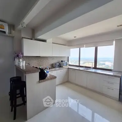Spacious modern kitchen with panoramic city view and sleek white cabinetry.