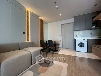 Modern living room with sleek furniture and integrated kitchen featuring a washing machine.