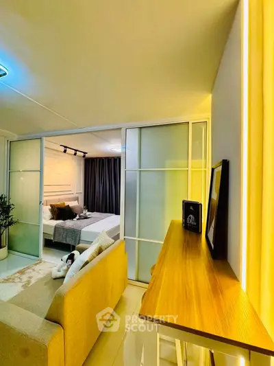 Modern apartment interior with cozy living room and stylish bedroom separated by sliding glass doors.