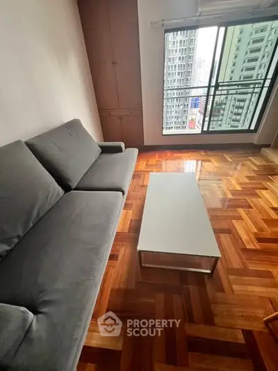 Spacious living room with parquet flooring and city view from large window.