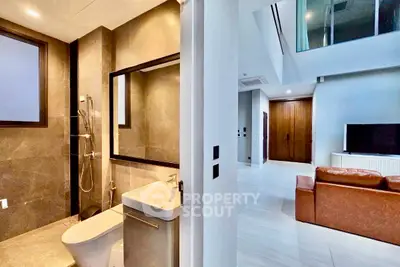 Modern apartment interior with sleek bathroom and spacious living area featuring leather sofa and large TV.